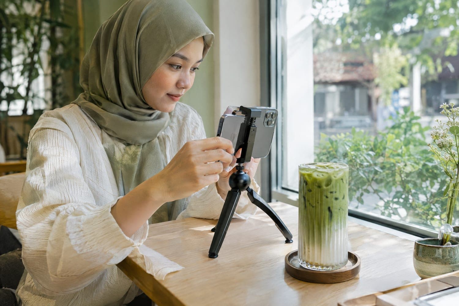 A content creator photographing an iced matcha latte with a phone on a tripod